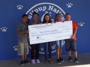 Lots of kids sitting outside with some holding a large check