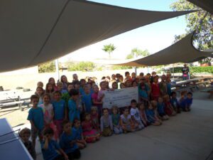 Lots of kids sitting outside with some holding a large check