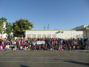 Lots of kids sitting outside with some holding a large check