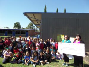 Lots of kids sitting outside with some holding a large check