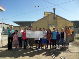 Lots of kids sitting outside with some holding a large check